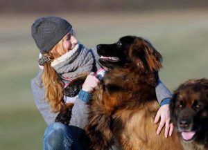 Frau mit Mütze und Schal spielt mit Ihren Hunden